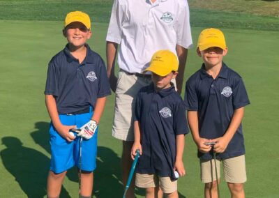 Golf staff member stands with young golfers on the green for a photo