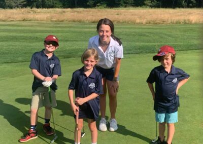 Golf staff team member poses with campers and their putters on the green