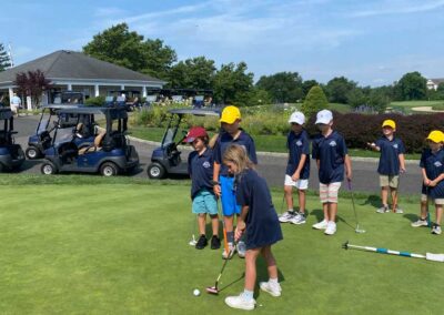 A group of young golfers watches a fellow golfer make a putt.